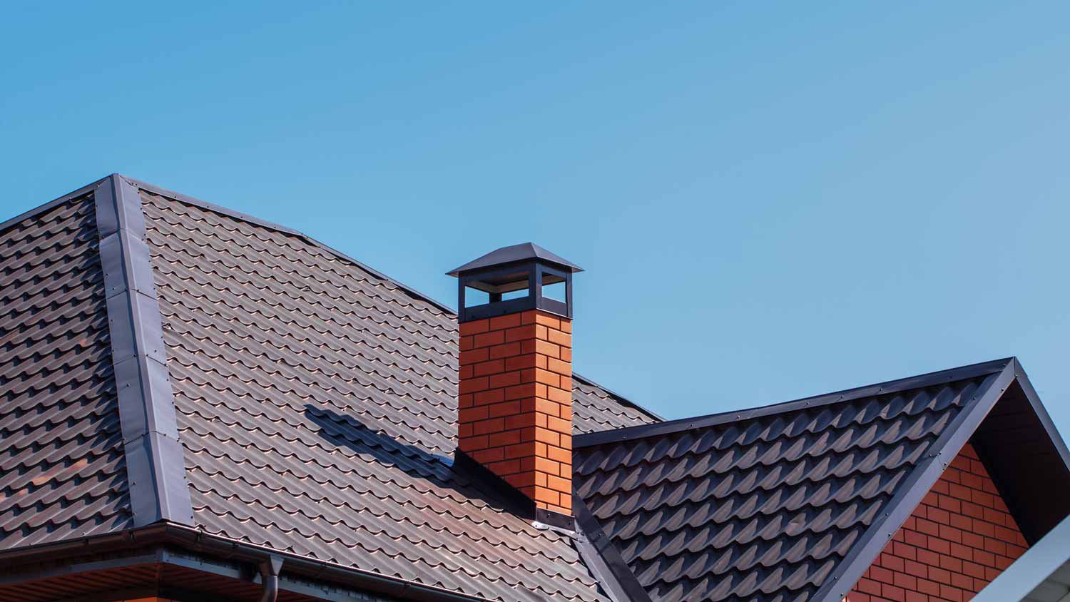 A brick chimney on a metal roof of a house