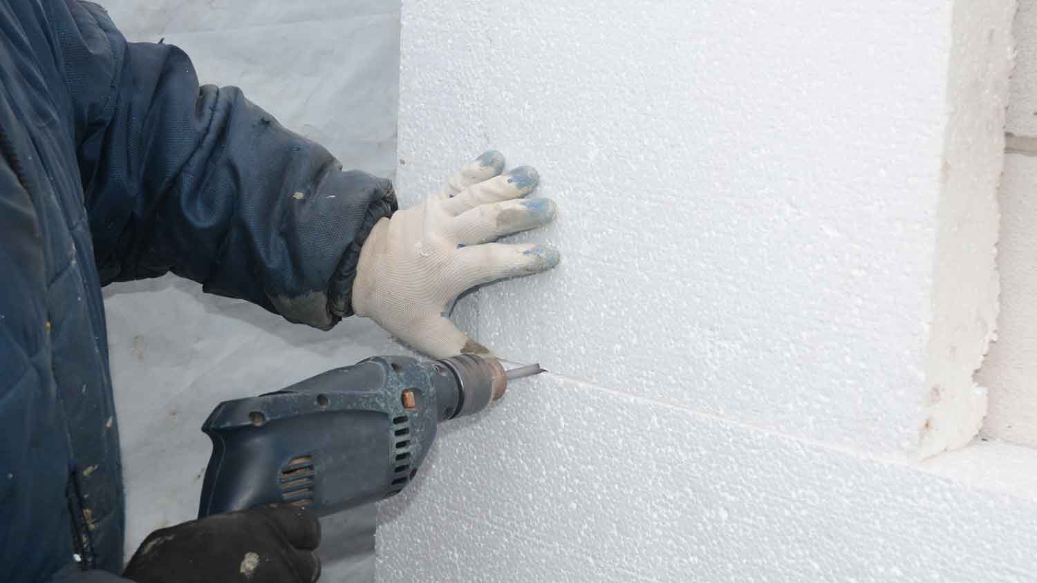 Worker drilling wall to install foam board insulation