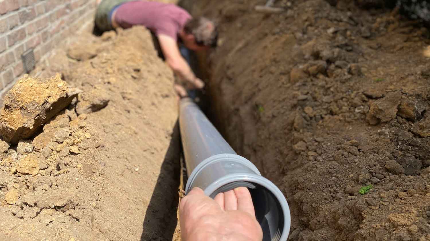 Professionals placing a drain pipe near a house’s foundation