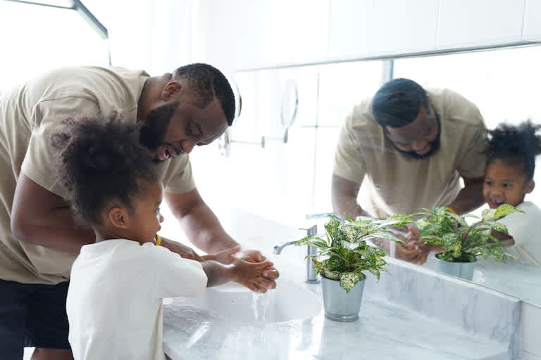father helping his young daughter was her hands in sink with marble countertop