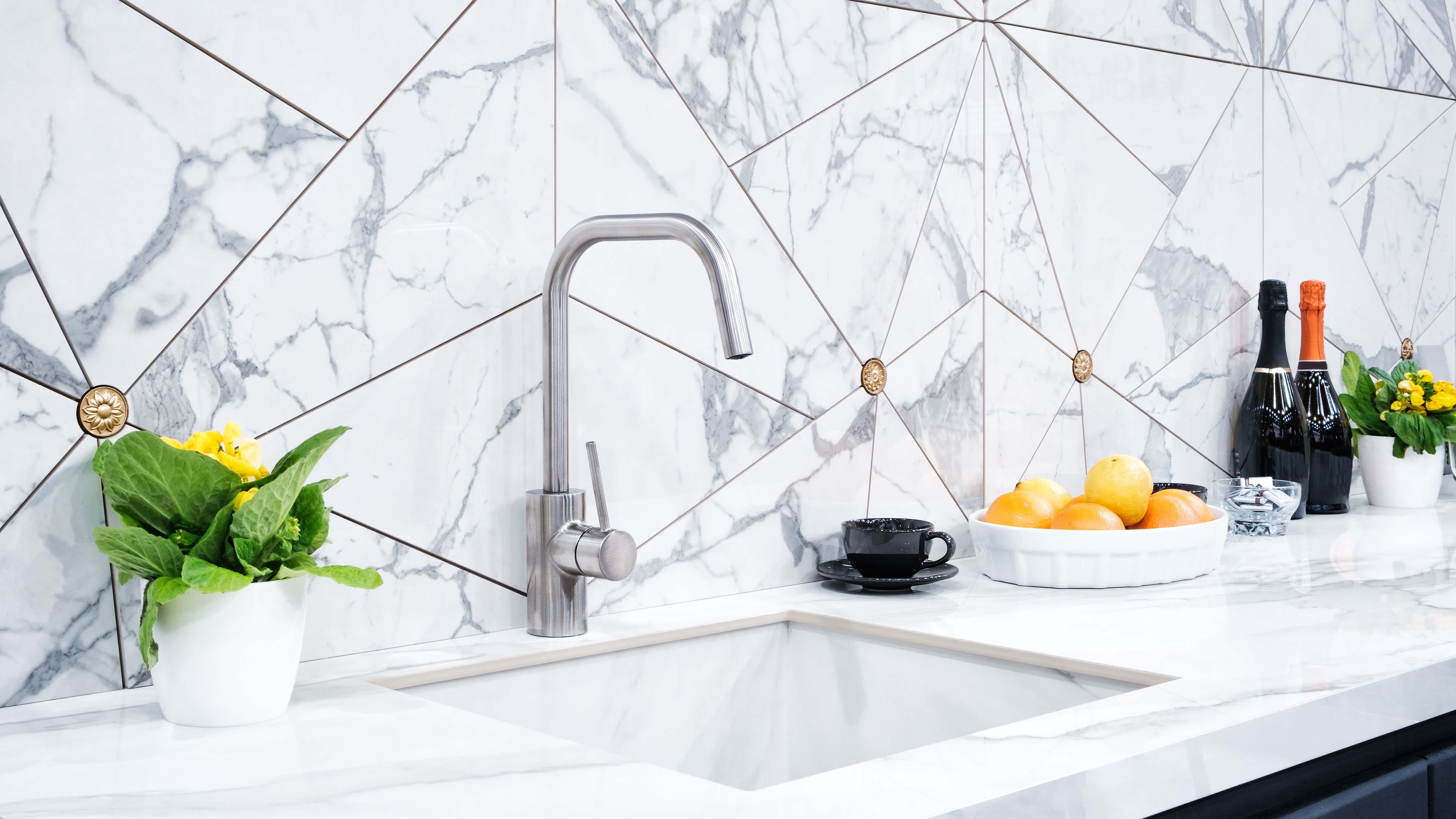 White marble kitchen countertop, kitchen sink, and white marble backsplash with triangle tiles and inlaid gold circles