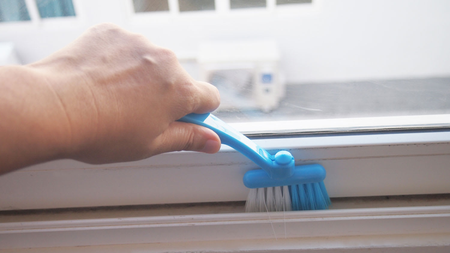 A person cleaning a window track with a brush
