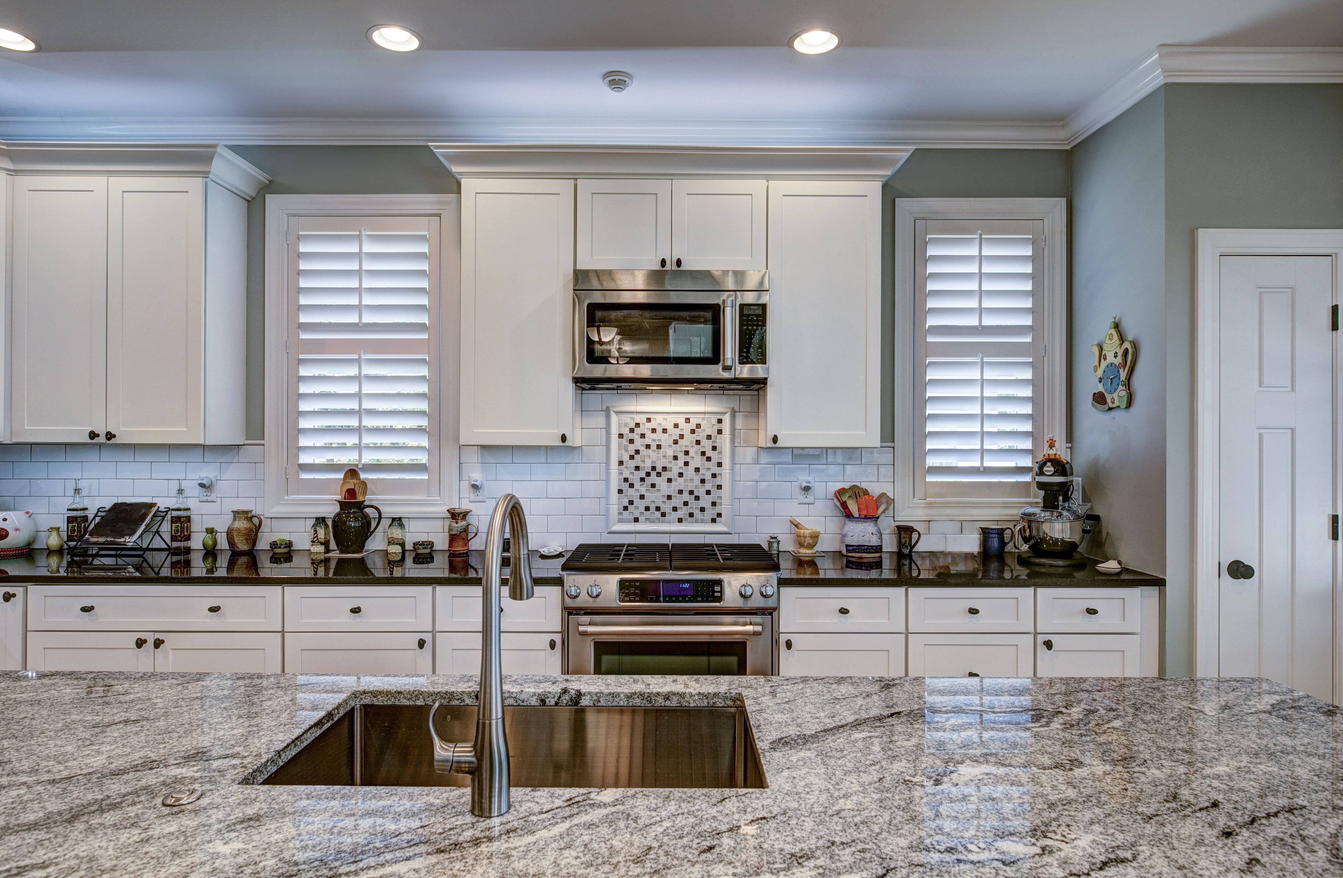 Luxury kitchen with gray granite island, white cabinets, black countertops, subway tile backsplash, and gray walls