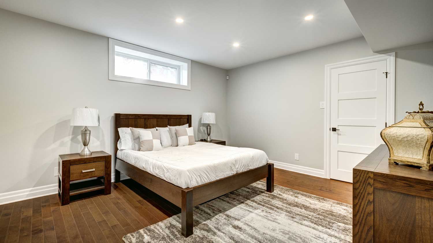 A basement bedroom with a hopper window above the bed