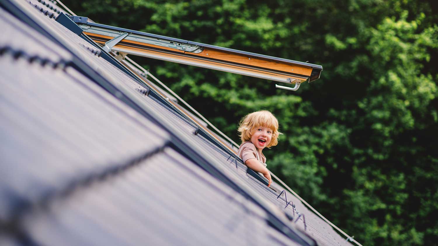 A smiling kid looking out a roof window