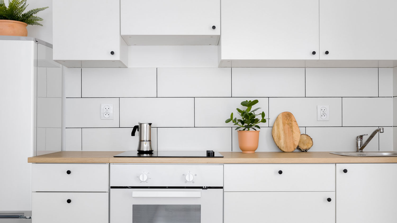A kitchen with white cabinets and backsplash with dark grout