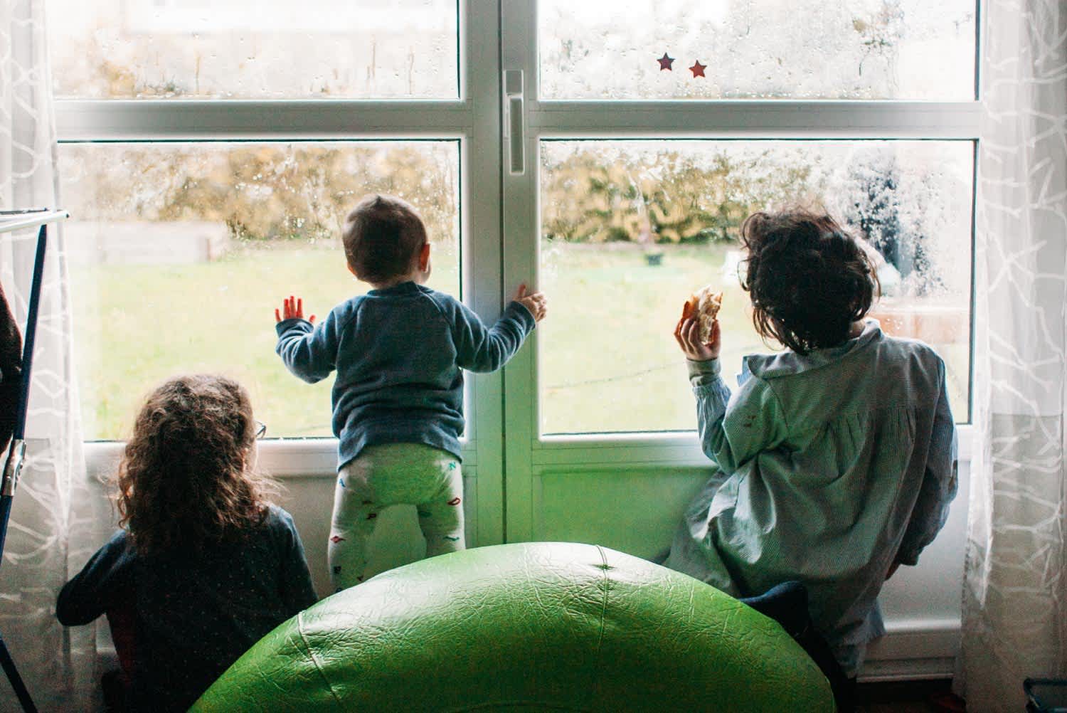 Three kids looking outside a foggy window