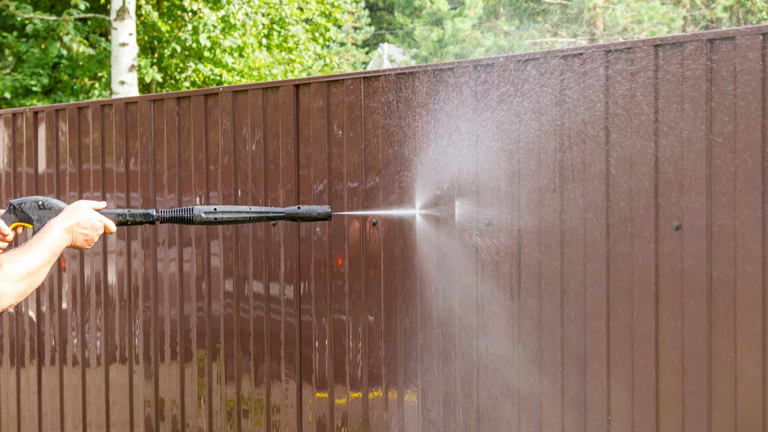 man cleaning fence with power washer