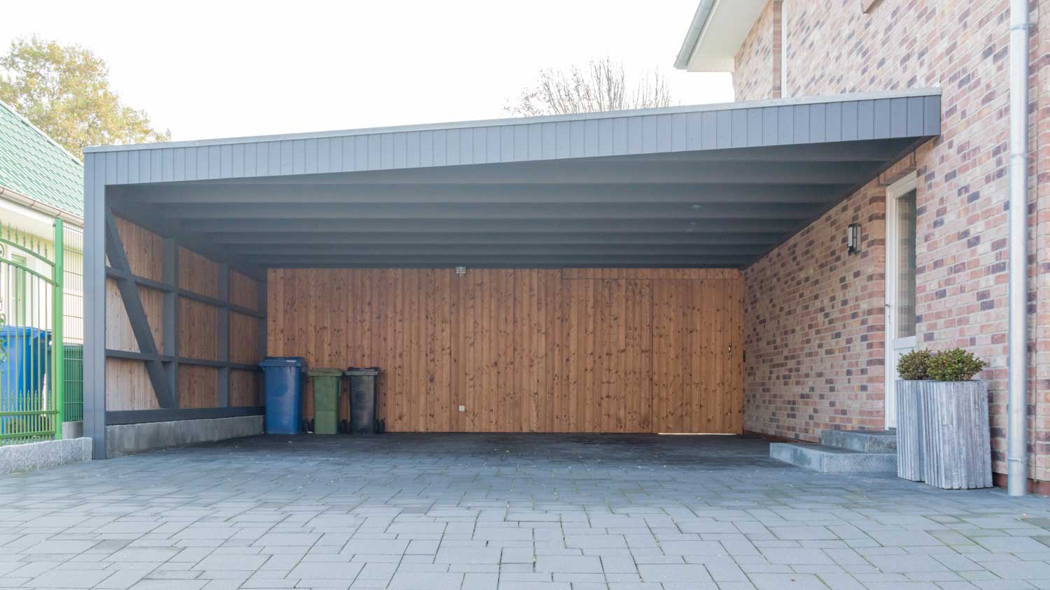 An enclosed carport with recycle bins in the background