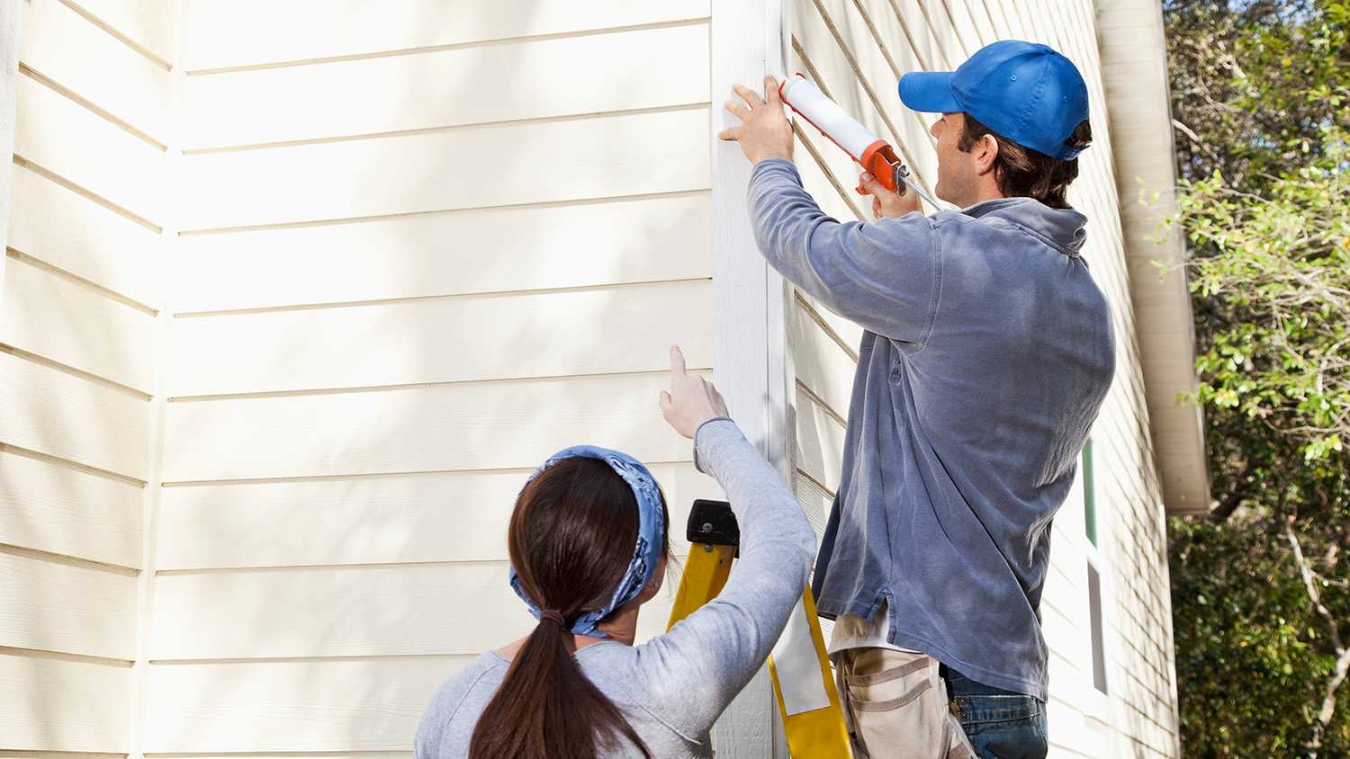 Man caulking siding on a ladder