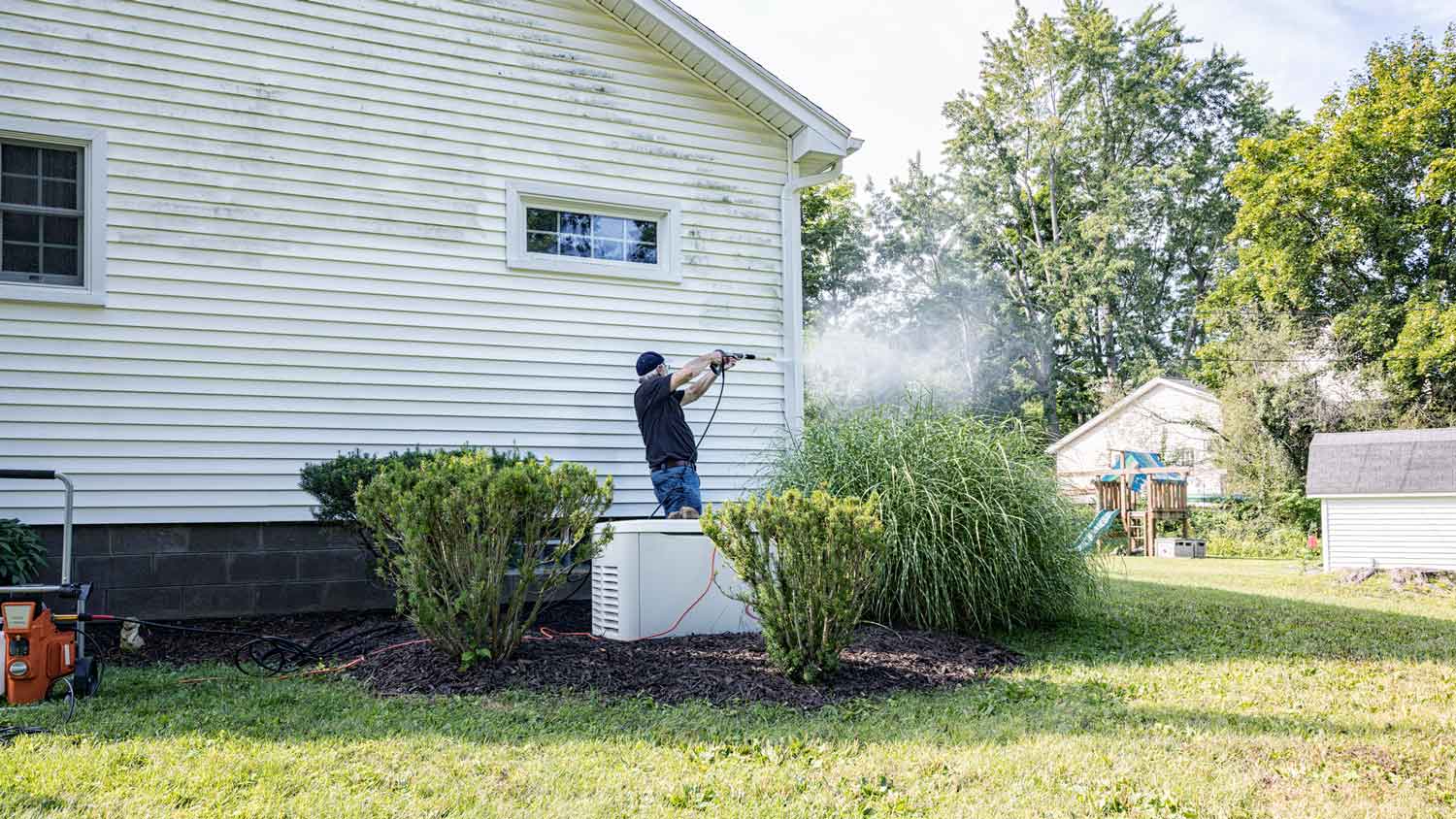 A senior man pressure washing the vinyl siding of his house