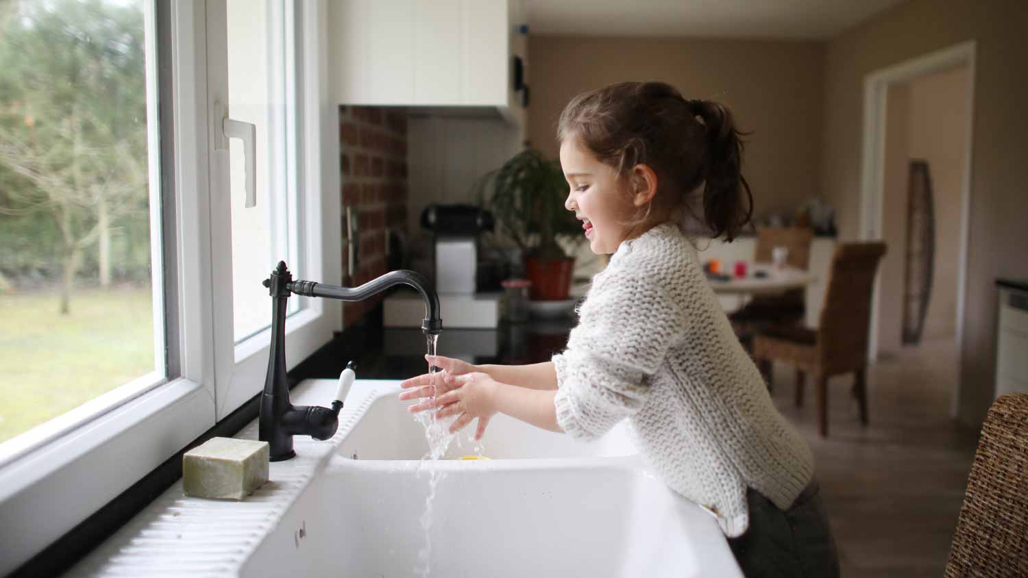 A little girl washing her hands in the kitchen with her mother