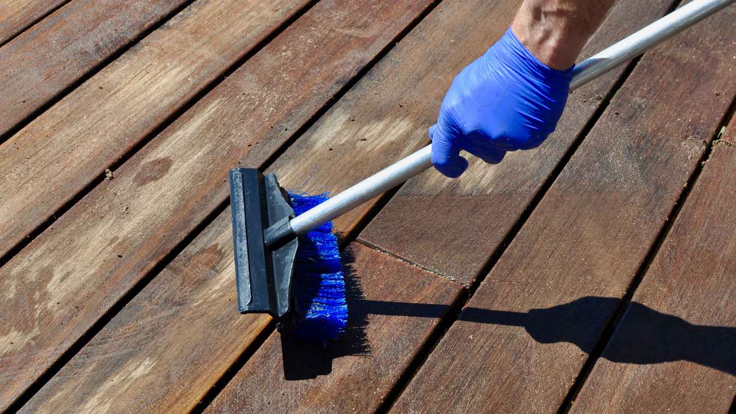 A person wearing protective gloves scrubbing a wooden deck