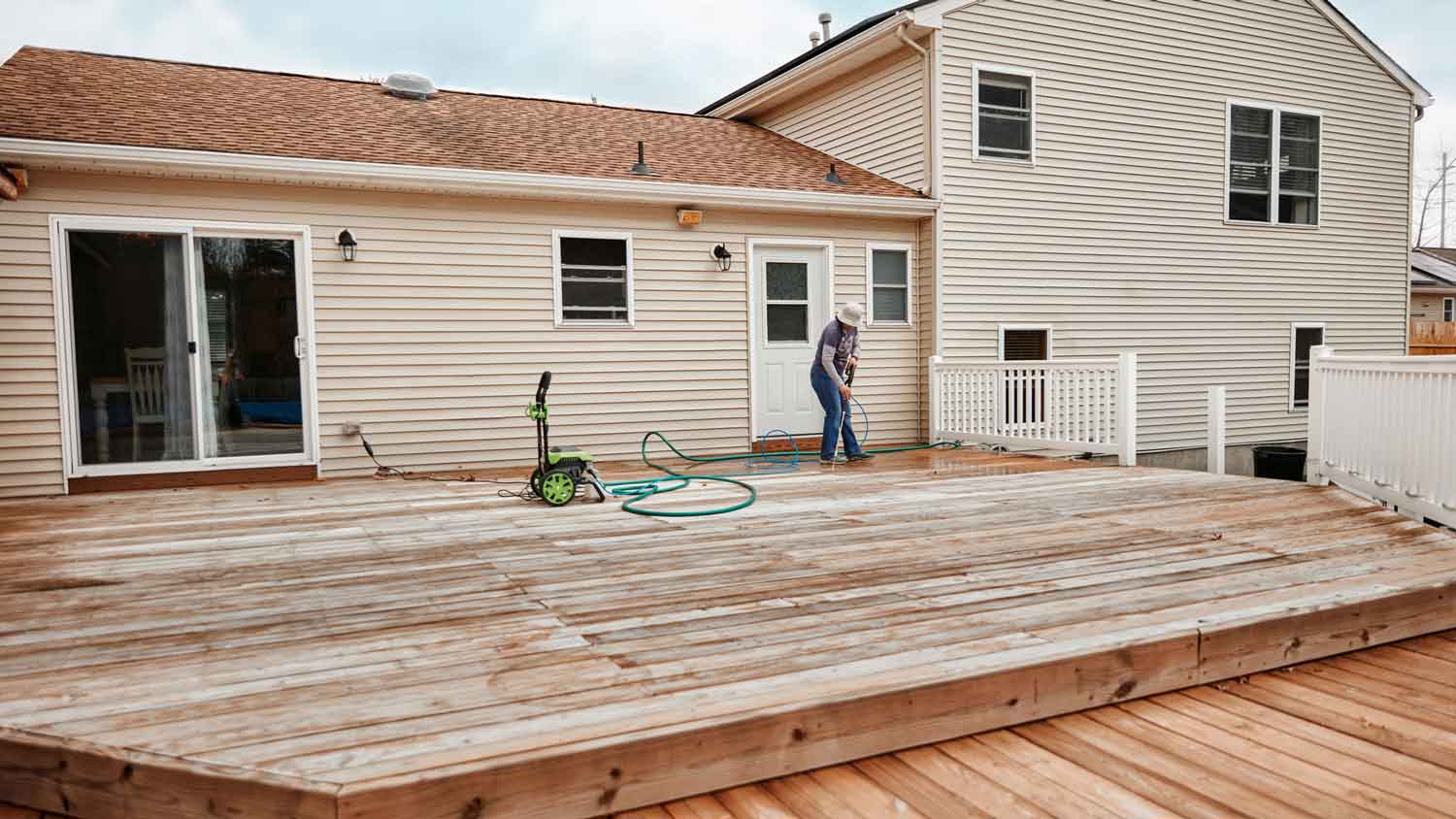 A woman using a pressure washer on her deck