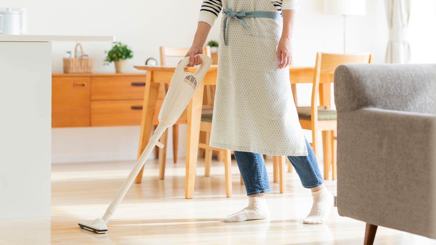 A woman cleaning the kitchen floor with a vacuum