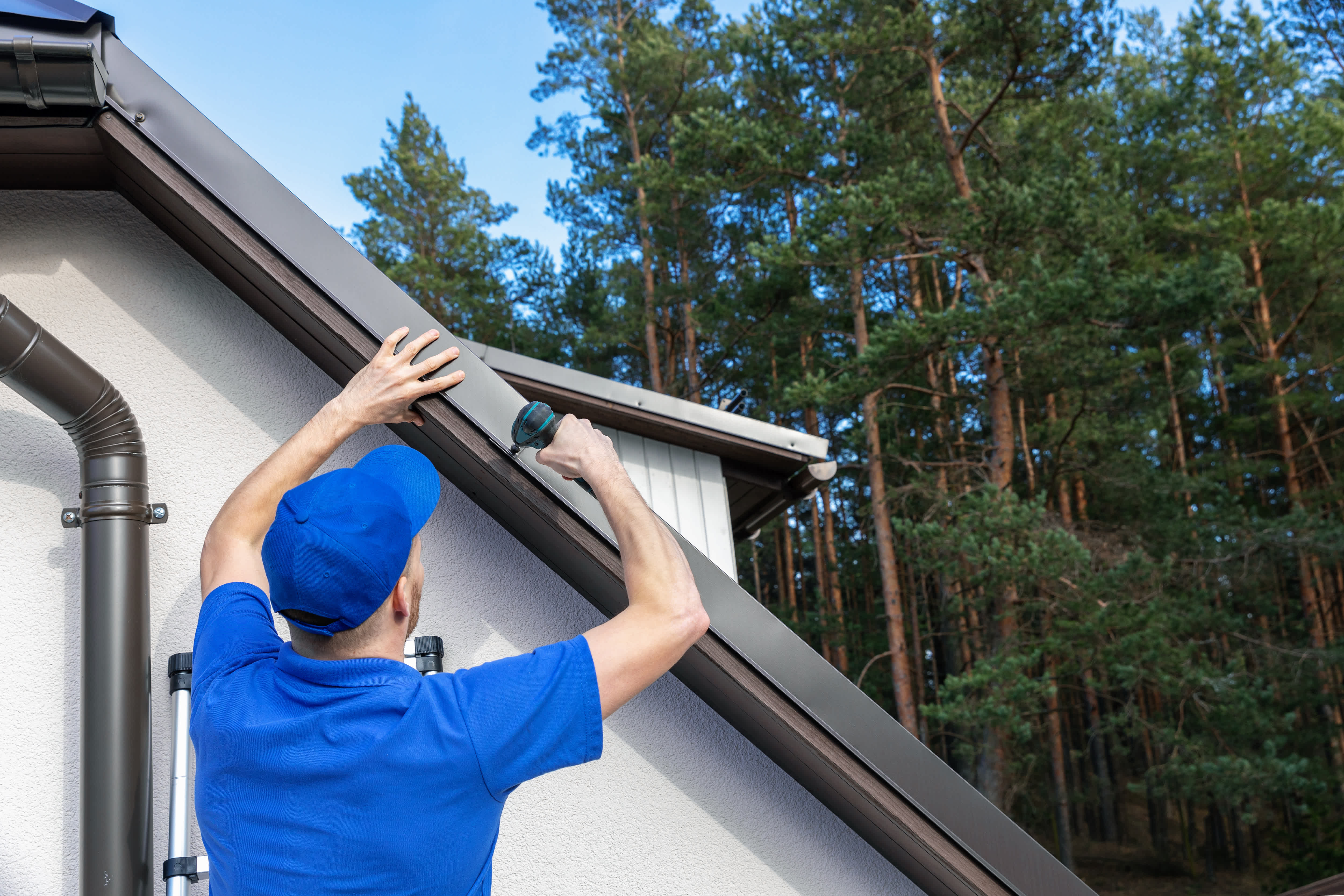 A roofer installing a metal drip edge along the side of a roof