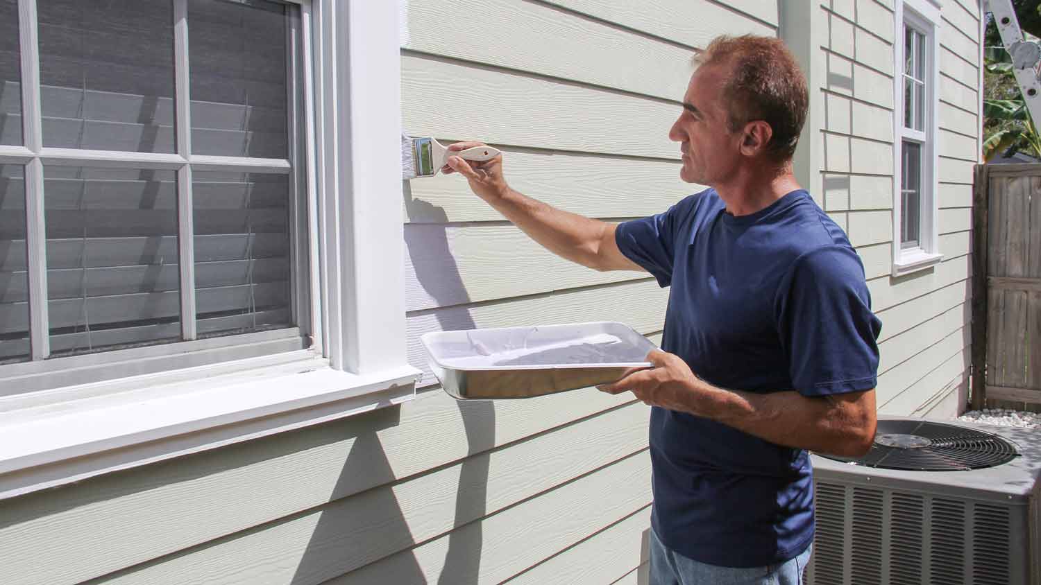 man painting siding with brush