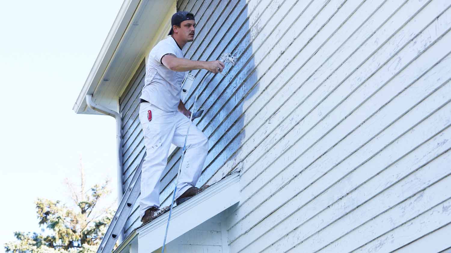 man spraying paint on vinyl siding