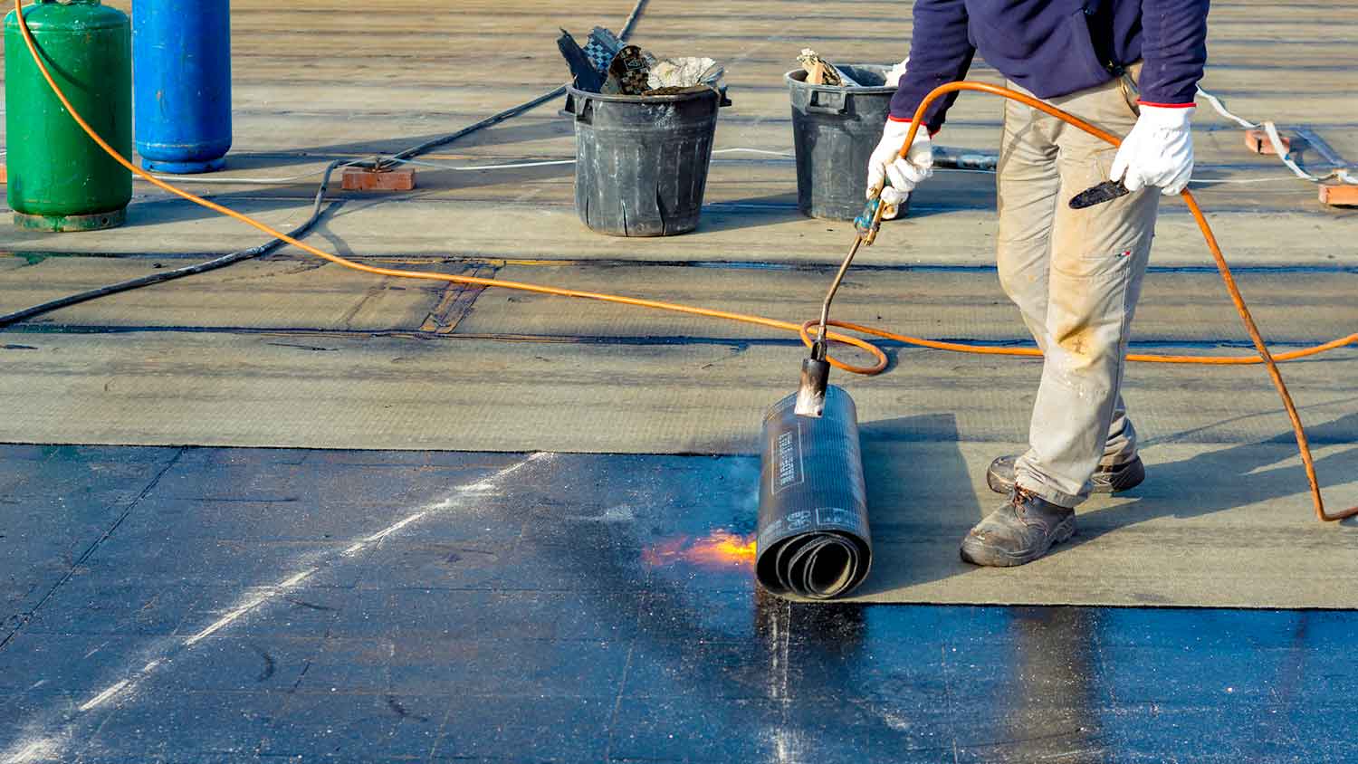 Worker installing bitumen sheets on a house roof