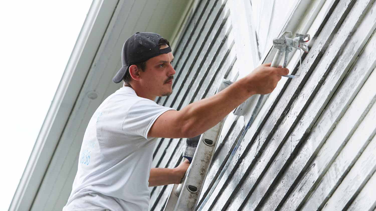 man spraying paint on house exterior