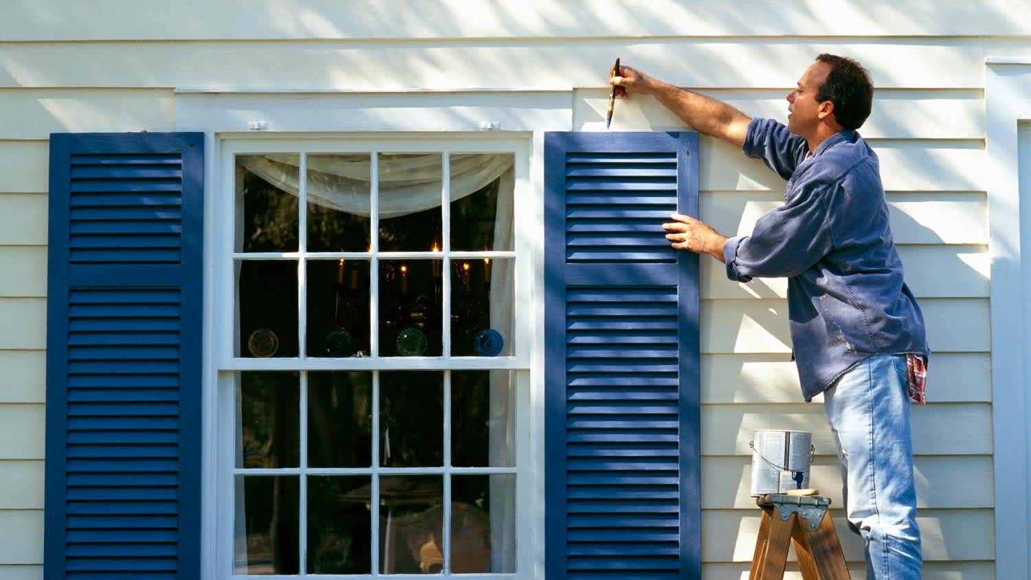 A man painting the exterior shutters of a house