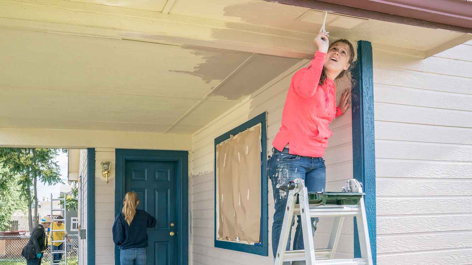 Woman on a ladder painting house porch