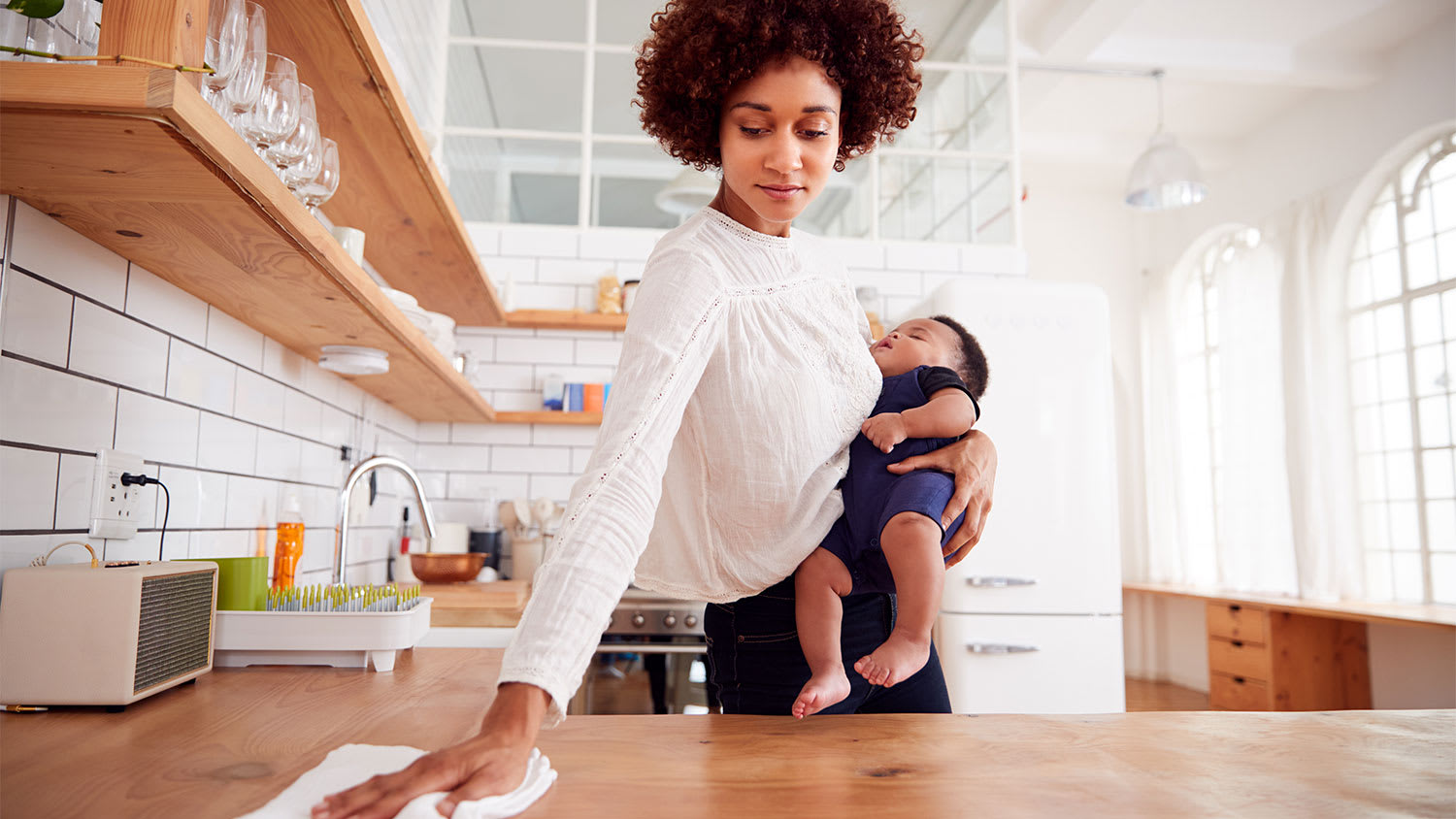 Woman holds her baby and cleans the kitchen
