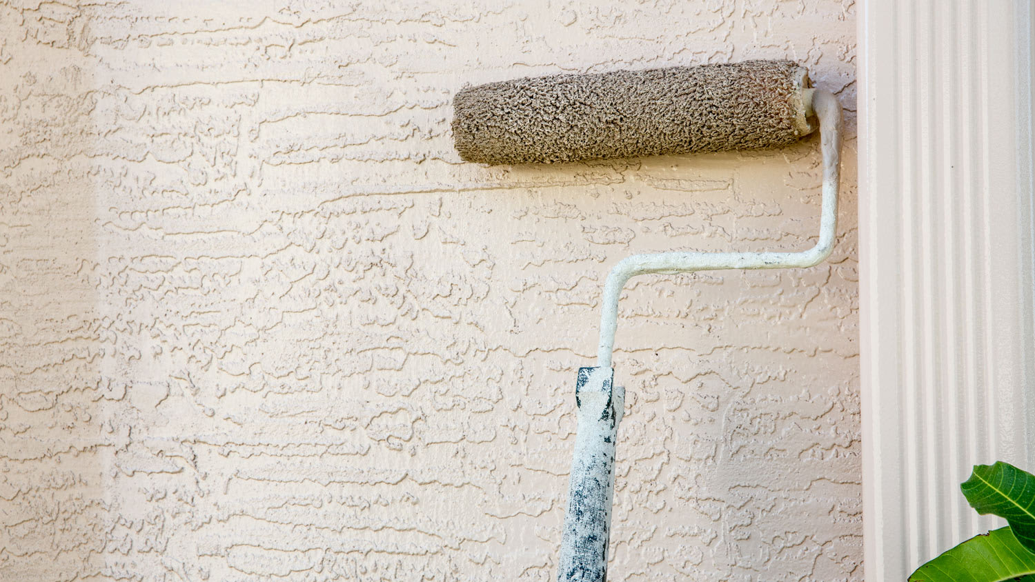 Paint roller attached to pole on outside wall of house