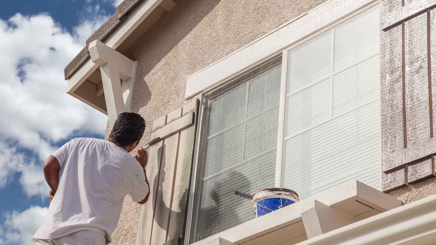 A man on a ladder painting shutters