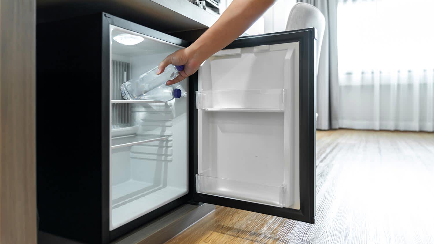 A person placing a water bottle in a mini refrigerator