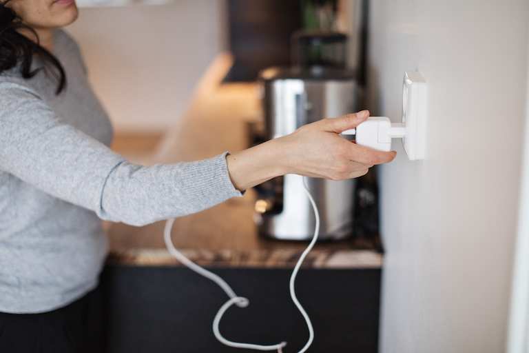shot of woman in gray shirt plugging in power cord of coffee pot to electrical outlet