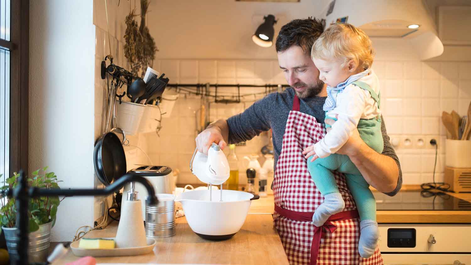 Father holding baby using electric mixer to make a cake