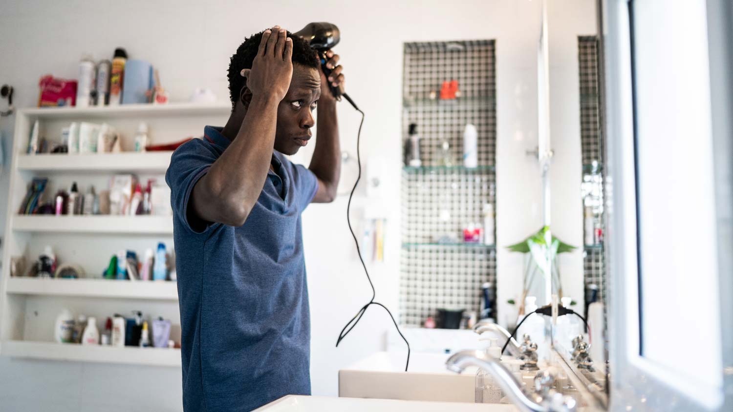 A young man blow drying his hair in the bathroom