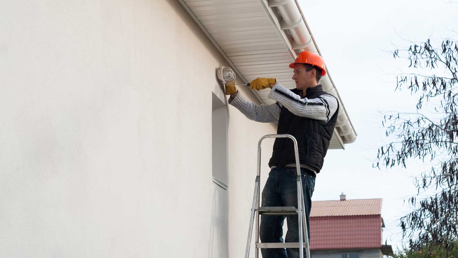 An electrician on a ladder installing outdoor lighting to a house
