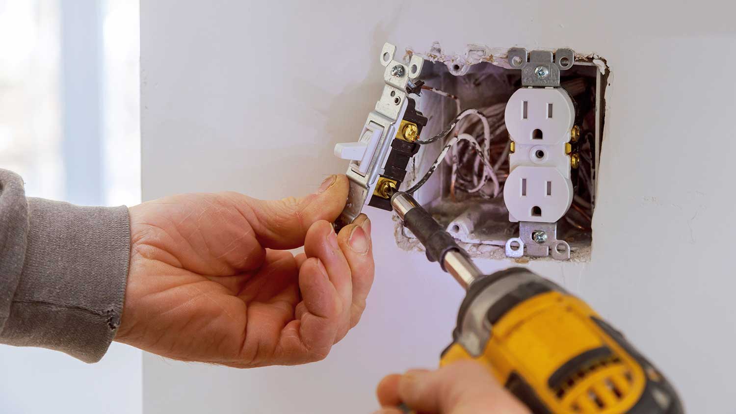 Electrician using electric screwdriver to wire a light switch