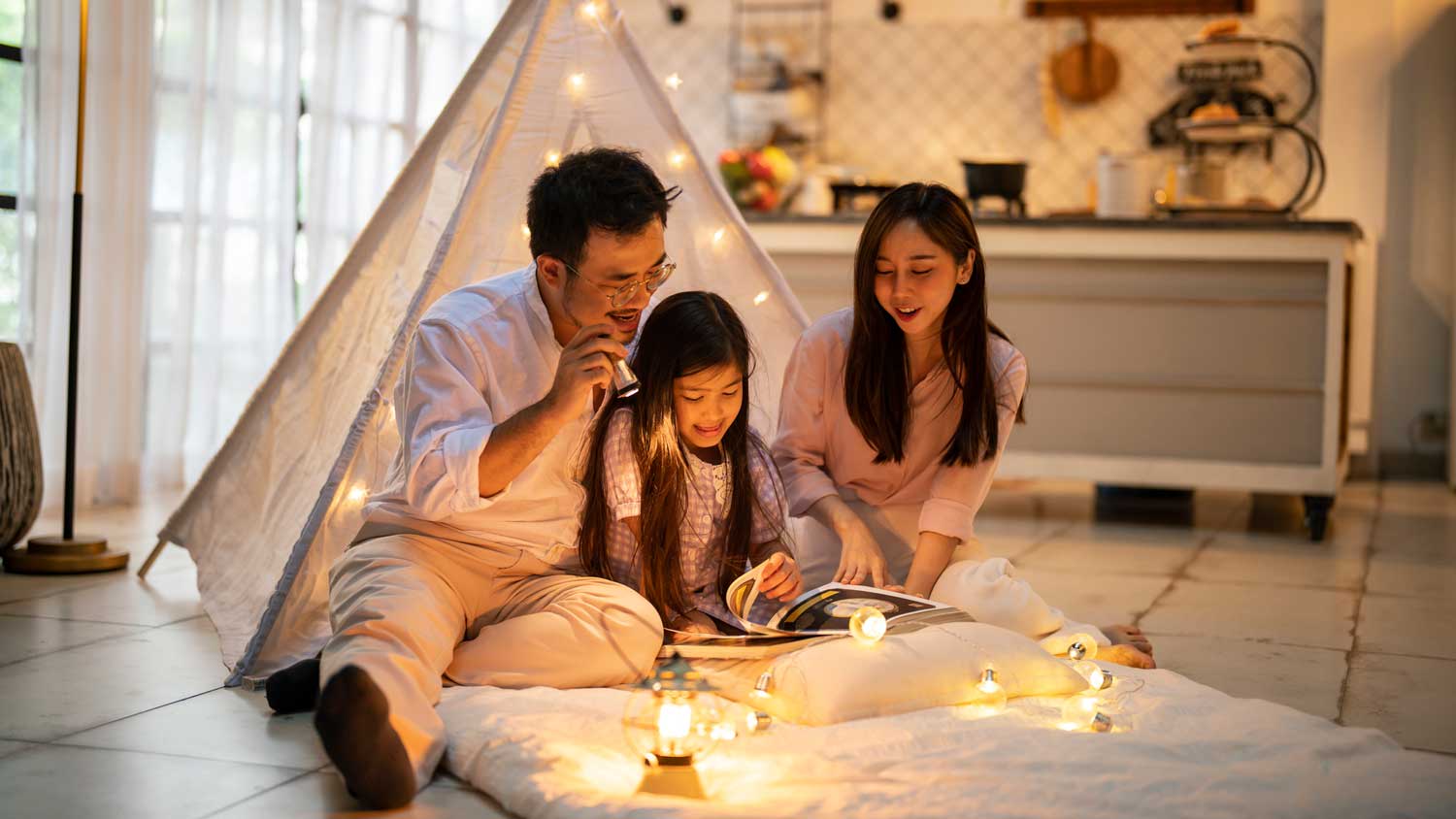 A family reading a book in front of a teepee tent