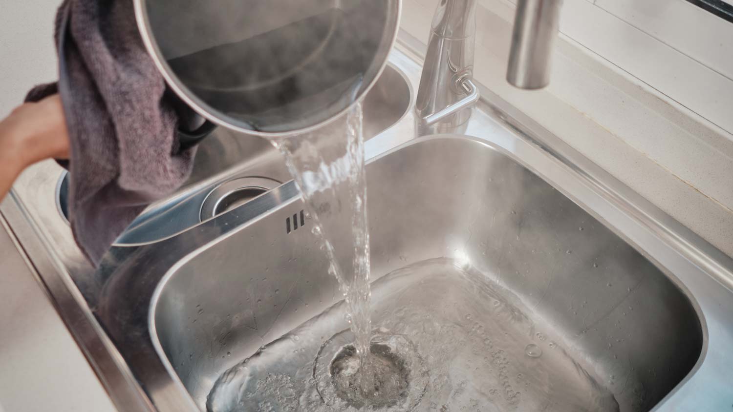 Pouring hot water from a pot to unclog a drain