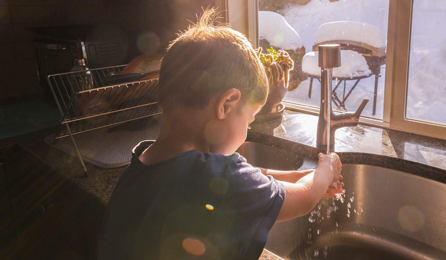 Little boy washes hands at kitchen sink, winter scene thru windows