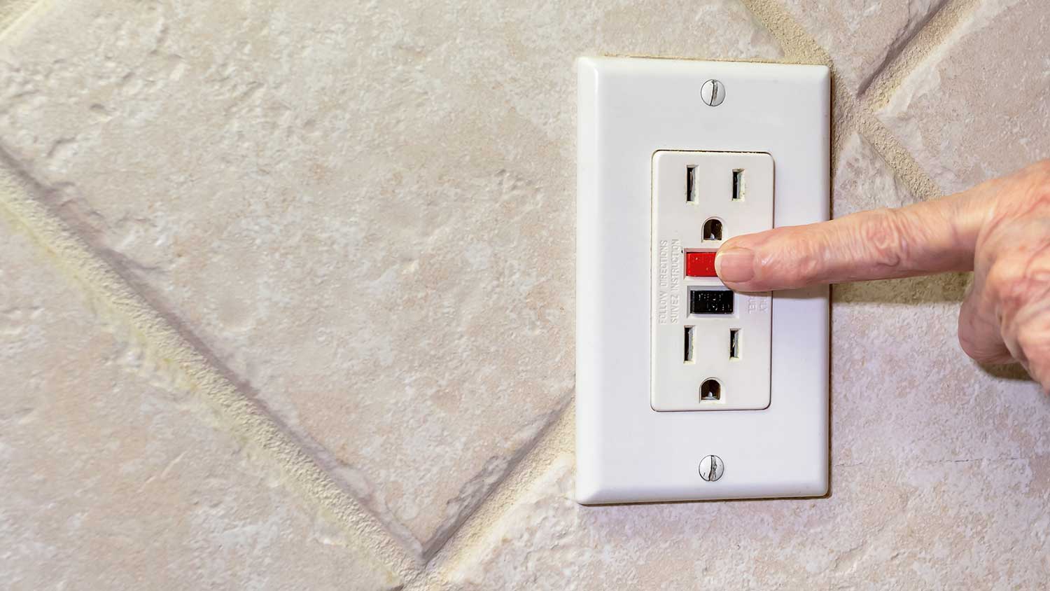 Hand pushing the reset button on a GFCI outlet