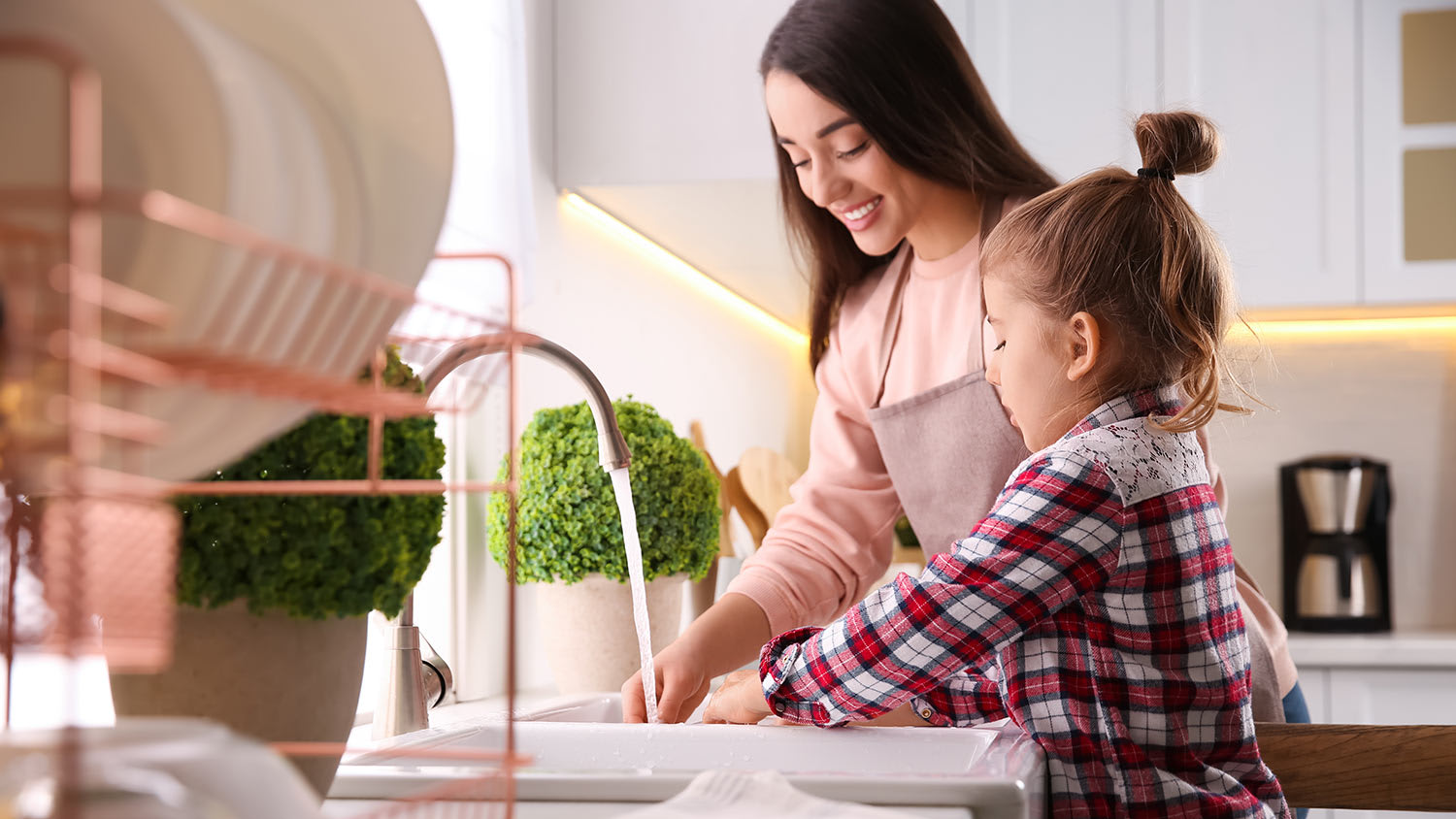 Mother and daughter wash dishes together in kitchen sink