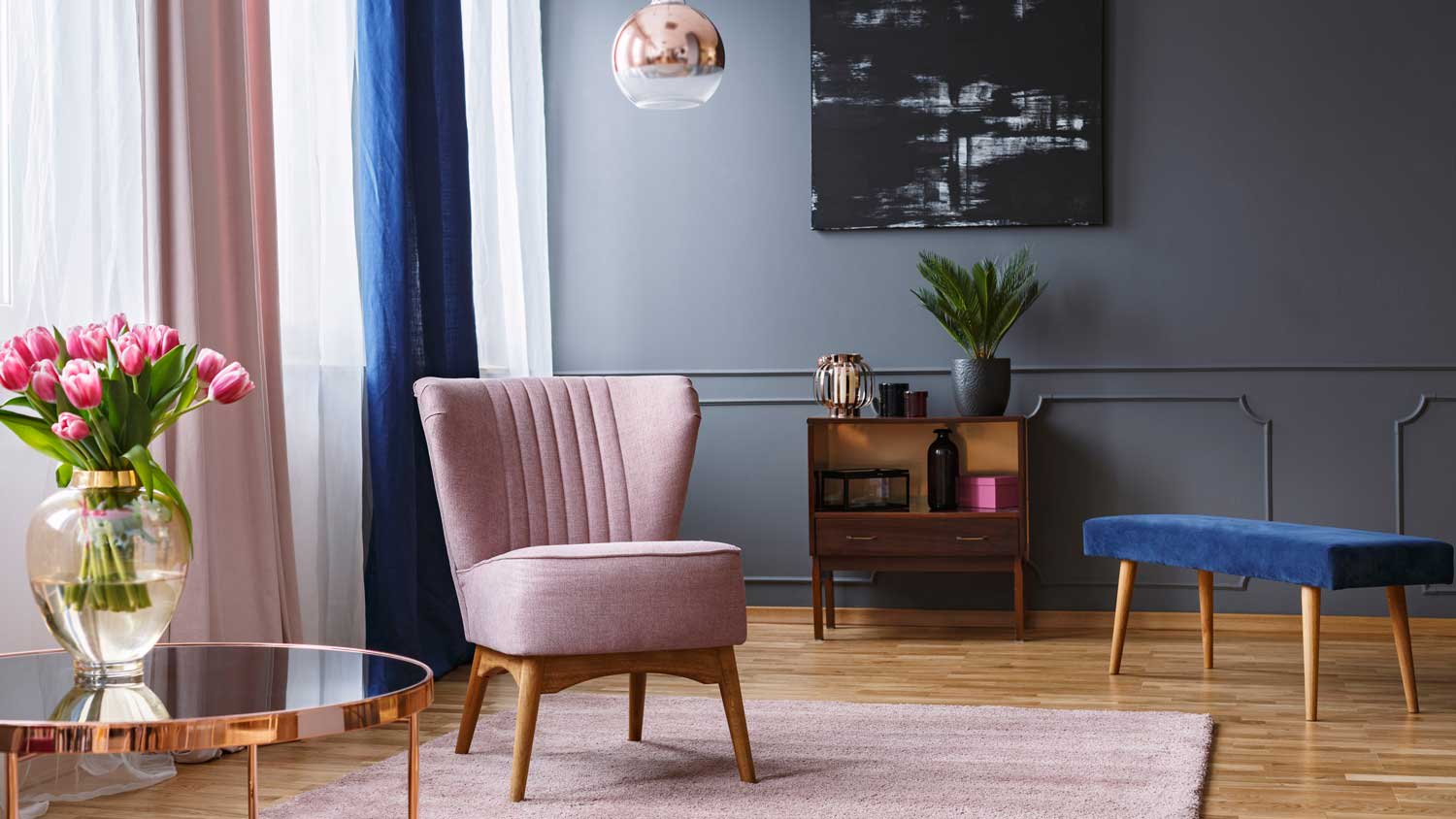 A pink armchair in a living room with dark gray walls