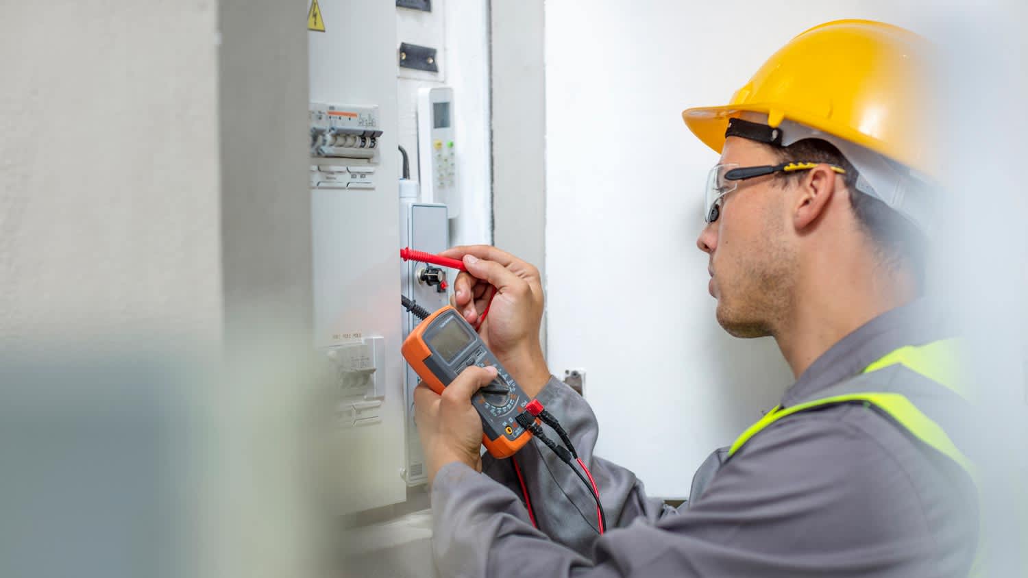An electrician working with a voltmeter in a fusebox