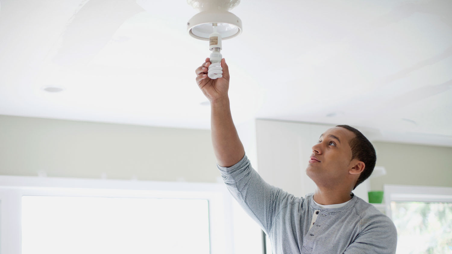 Young man replacing lightbulb on a ceiling light fixture