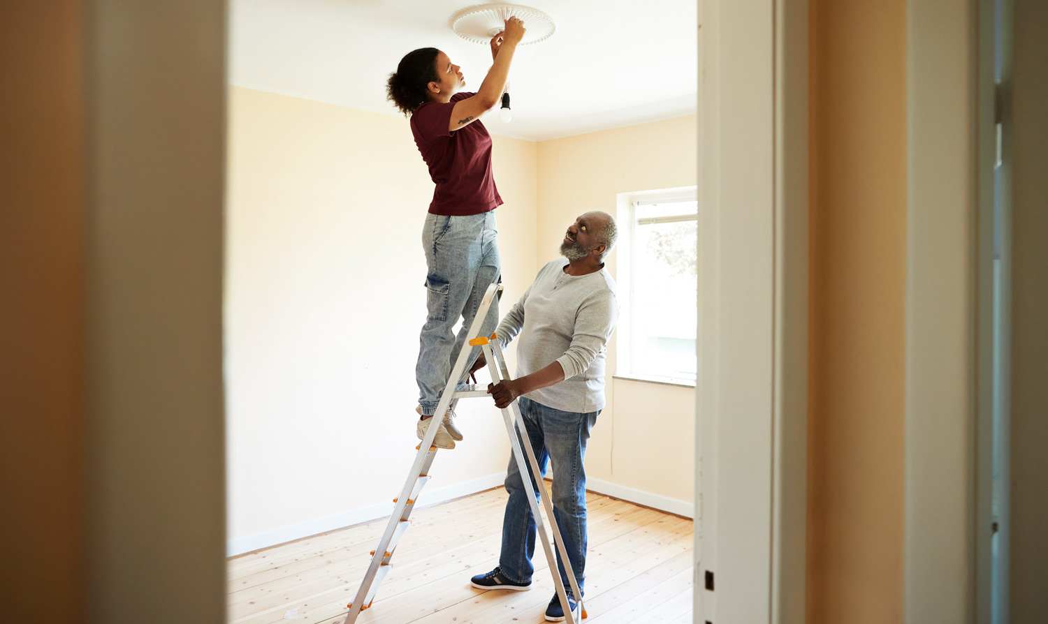 A woman installs a light bulb while her father holds the ladder