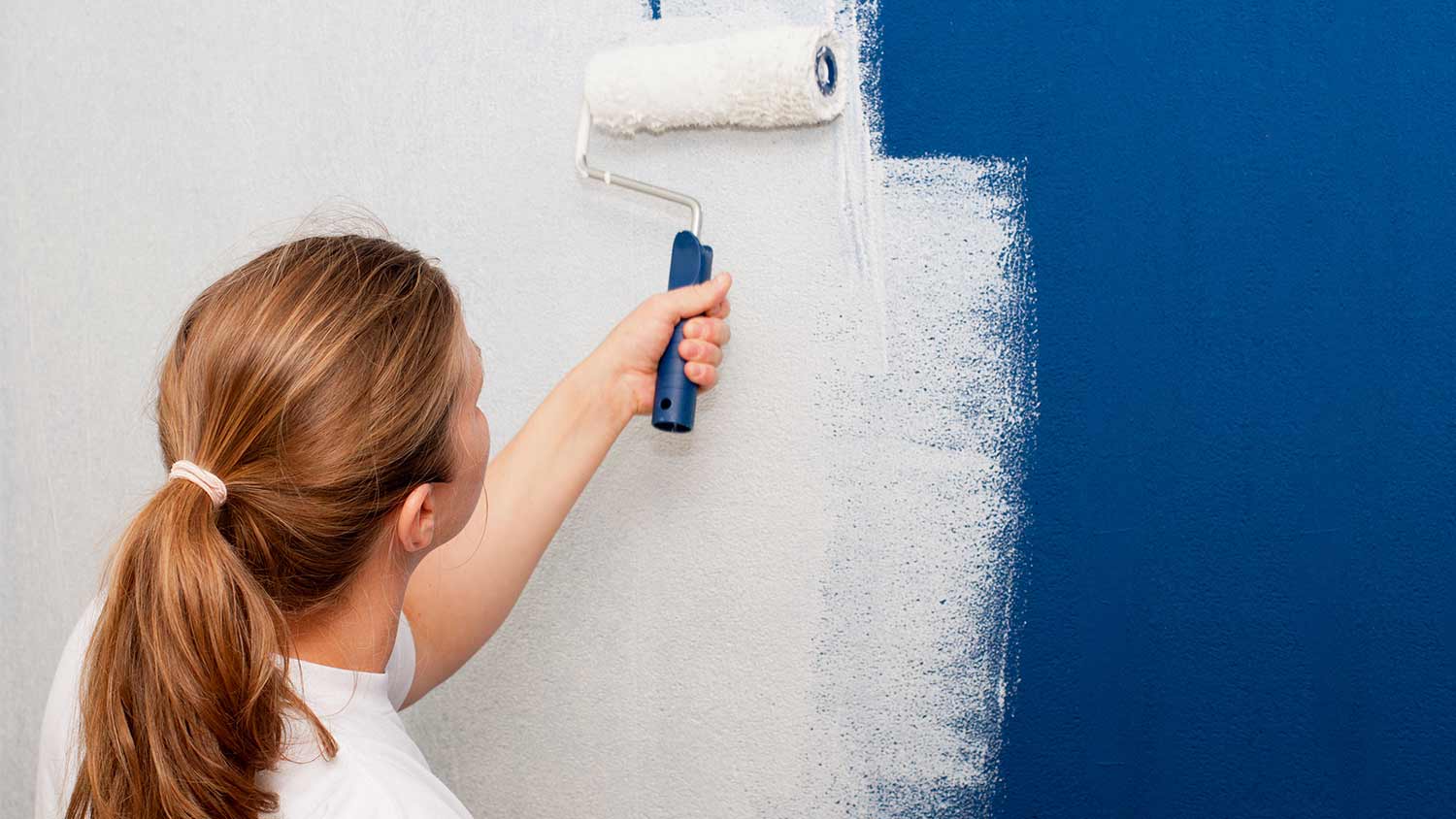 woman painting over blue wall with primer