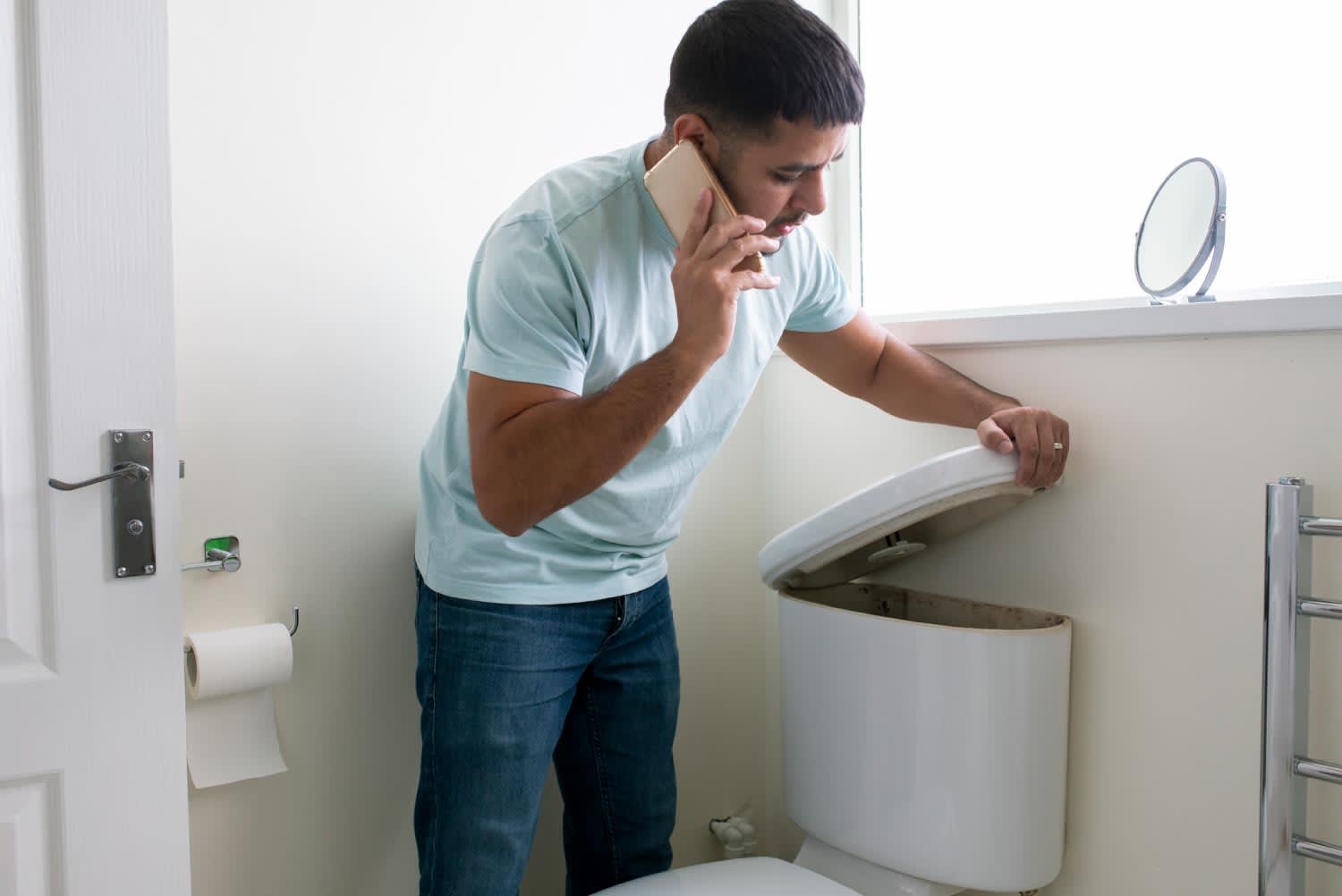 A man in his bathroom calling a plumber
