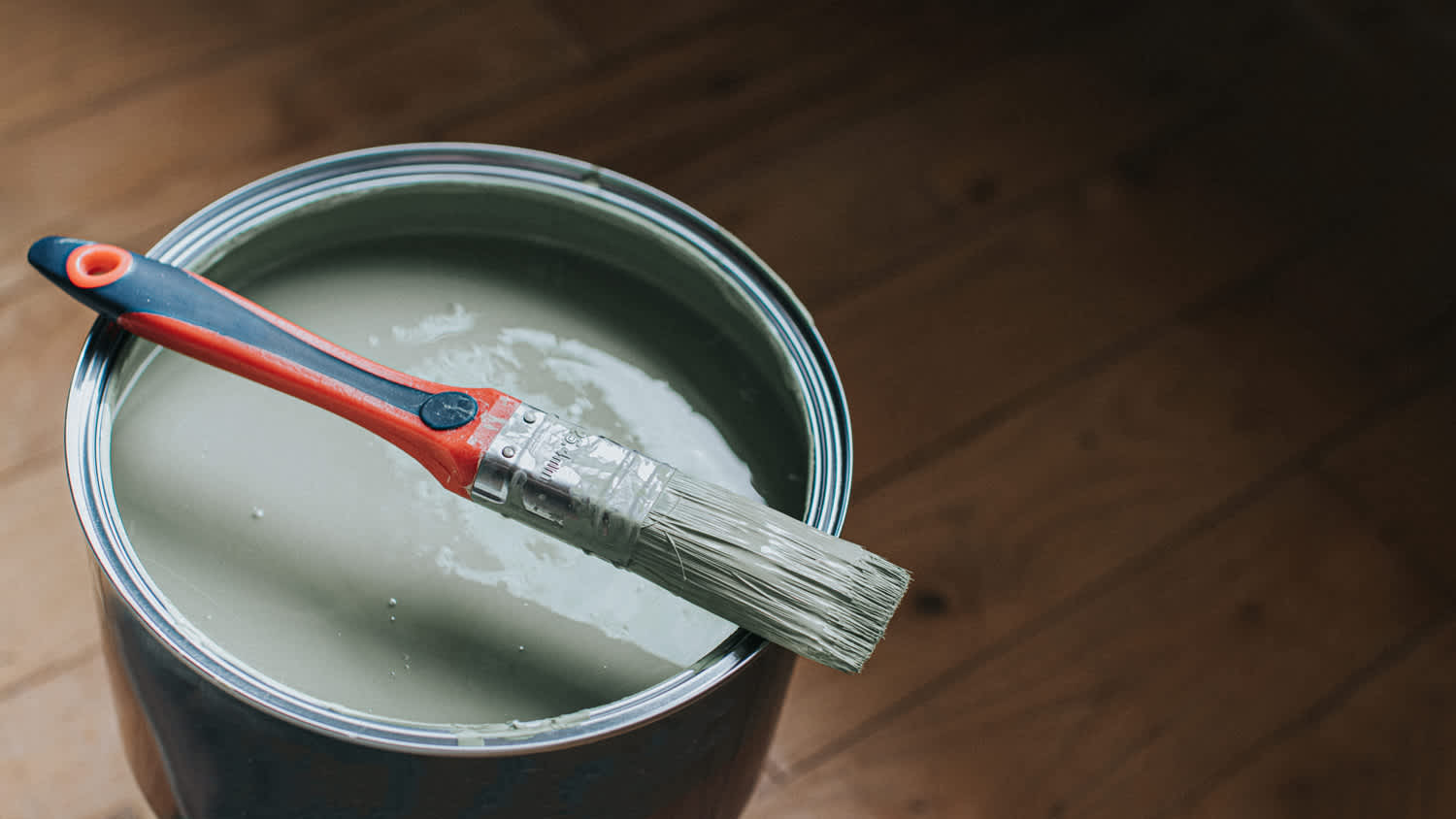 A small paintbrush sits on top of a large tin of paint.