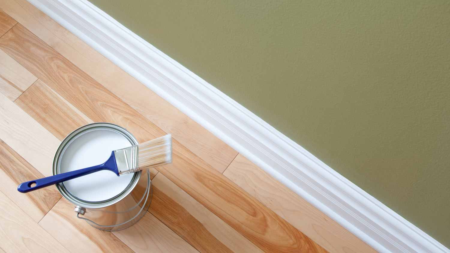 Paintbrush and a can of white paint on floor