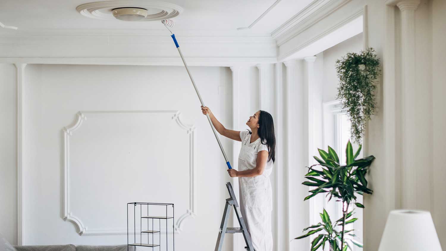 Woman on a lather painting living room ceiling