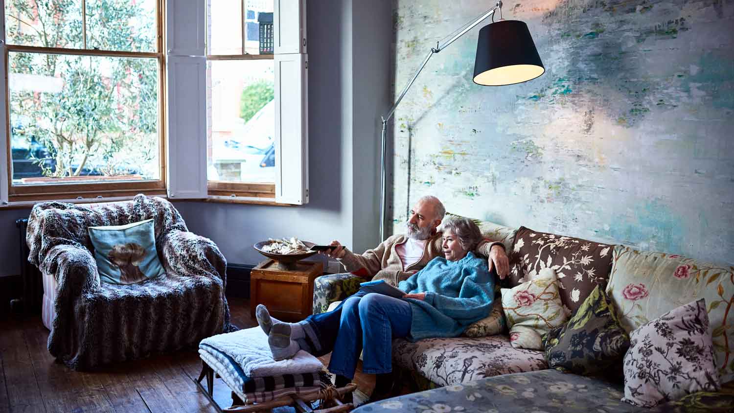A senior couple watching TV in their living room with an antiquing wall on their back